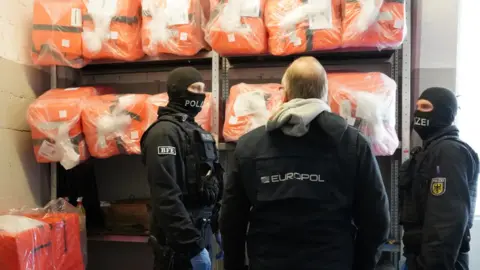 La policía de Europol se encuentra junto a estantes llenos de equipos