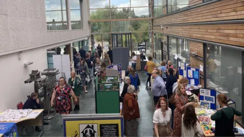 West Northamptonshire Council Foyer of office building with trees visible through window and large crowd of people inside.