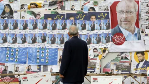 EPA A man looks at electoral posters on a wall in Tehran, Iran (28 February 2024)