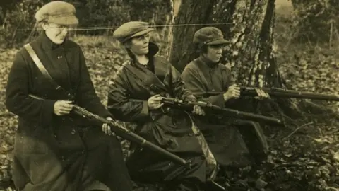 UCD Archives/EITHNE COYLE O’DONNELL PAPERS/P61/9 Linda Kerns, Eithne Coyle and Mae Burke at rifle practice in Duckett’s Grove, Carlow