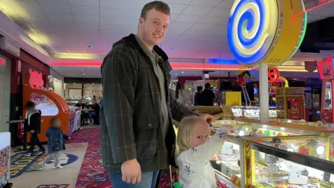 Tom Seadon with daughter Katie playing a 2p coin tipper machine at Lyons Robin Hood Holiday Park in Rhyl, Denbighshire