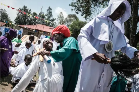 AFP Woman dressed in religious clothing falling back with a pained expression. She is being held up by man who has a cross in his hands.