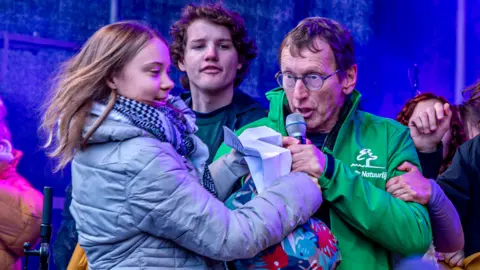 A man grabs the microphone from Greta Thunberg at a large climate protest in Amsterdam