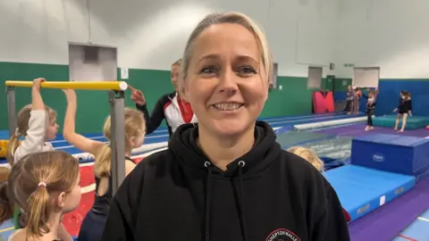 Clare Tanner smiling with children in the background doing gymnastic moves