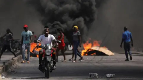 Reuters A man drives past a burning barricade during a protest against Prime Minister Ariel Henry's government and insecurity, in Port-au-Prince, Haiti March 1, 2024