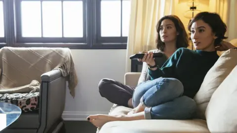 Getty Images Sisters watching TV on sofa at home