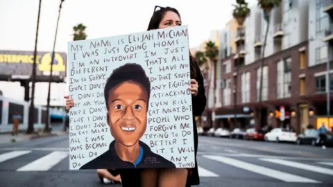 Getty Images A woman holds a sign at a candlelight vigil for Elijah McClain in California in 2020