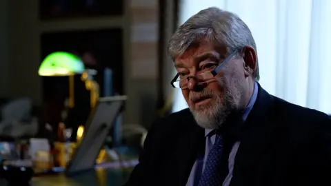 Konstantin Remchukov, Chief Editor, Nezavisimaya Gazeta, sits in front of a desk.