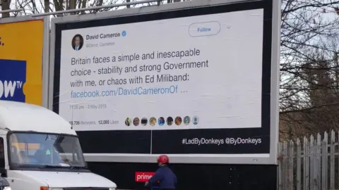 Led By Donkeys A tweet by former Prime Minister David Cameron reading "Britain faces a simple and inescapable choice - stability and strong Government with me, or chaos with Ed Miliband" is on a billboard next to the A10 in London