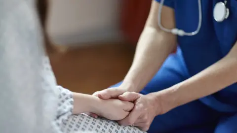 Getty Images Nurse holding a patients hand