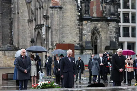 Reuters German President Frank-Walter Steinmeier (R), Britain's King Charles III (C), and Hamburg's Mayor Peter Tschentscher (L) pay their respects during a wreath-laying ceremony during their visit to the St Nikolai Memorial Church in Hamburg, northern Germany on March 31, 2023.