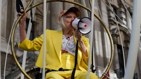 AFP Vivienne Westwood speaks into a megaphone while dressed in yellow in a bird cage
