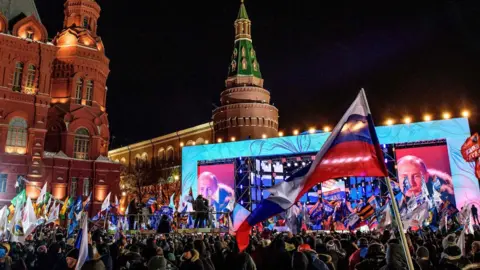 AFP People listen to presidential candidate, President Vladimir Putin during a rally and a concert celebrating the fourth anniversary of Russia"s annexation of Crimea at Manezhnaya Square in Moscow on March 18, 2018.