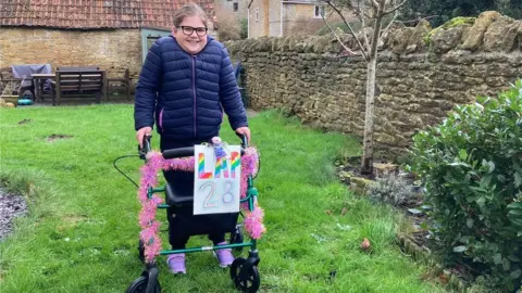 BBC Emily in her garden, standing with a walking aid