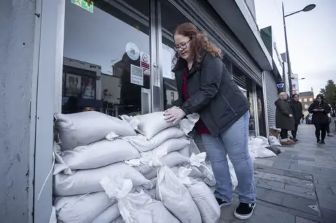 PA Media A woman stacks sandbags outside a shop in Downpatrick