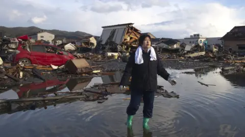 Getty Images A woman stands in water amidst tsunami wreckage