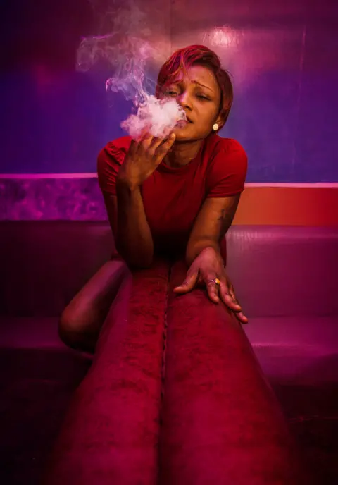 Antoine Ngolké Doo Woman smokes a cigarette and seductively leans on a red leather sofa