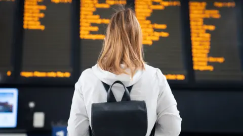 PA Media Woman stands in front of train notice board