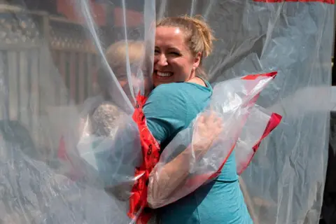 Jorge Uzon / AFP Two women hug through a clear plastic sheet