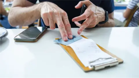 Getty Images A man's hand puts a credit card on a restaurant bill