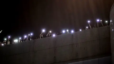 Getty Images Employees of the Apple Daily newspaper shine phone torches from their office rooftop during heavy rain and shout thanks to supporters down