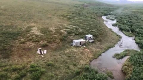 US Coast Guard Aerial view of shack encampment by a river where the man signalled for help