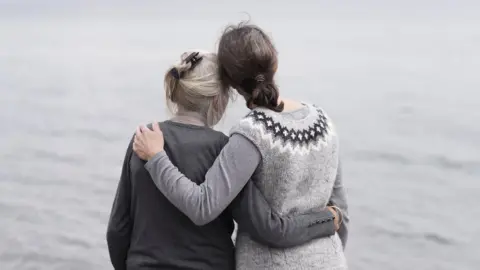 Getty Images Older and younger woman embracing by the sea - posed by models