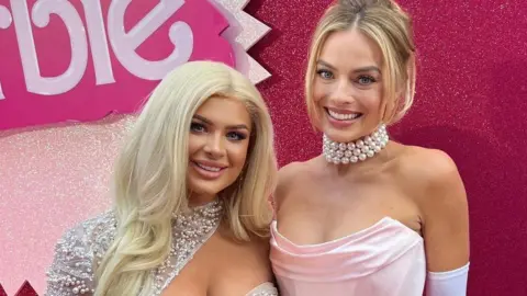 Liberty Poole Liberty Poole and Margot Robbie, smiling at the camera. Liberty is wearing a silver dress and Margot is in a pink dress