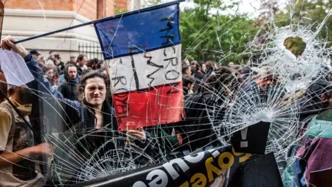 EPA A protester holds the French Tricolour with an anti-Macron slogan outside a destroyed McDonald's