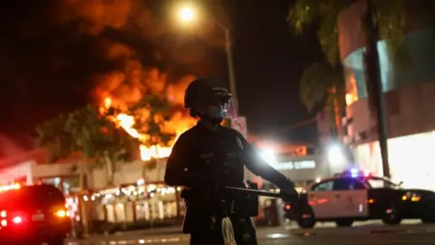 Reuters Police are deployed as a fire burns in Los Angeles, which is under curfew