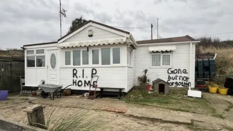 Andrew Turner/BBC Graffiti has been scrawled on one of the homes due for demolition