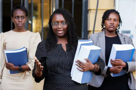 Reuters Three lawyers hold their documents and face reporters outside a courthouse.