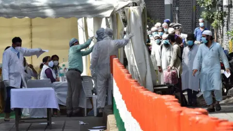 Getty Images People who took part in a Tablighi Jamaat function earlier this month are checked by a health team before being taken by bus to a quarantine facility amid concerns of infection.