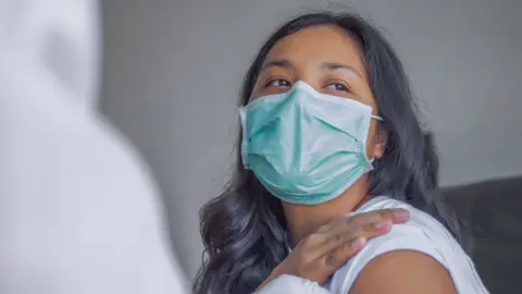 Getty Images Woman rolls us up her sleeve for the vaccine