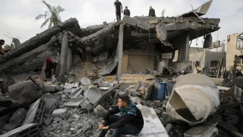 EPA Palestinians search for casualties beneath the rubble of a building destroyed in an Israeli air strike in Deir al-Balah, in the central Gaza Strip (8 December 2023)