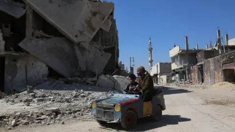 AFP A Syrian man drives a home-made toy car through Beit Naim in the Eastern Ghouta on 7 March 2017