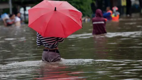 Getty Images Person standing with umbrella in flooded street