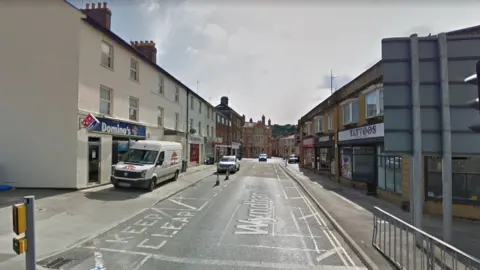 Google Maps A road with several shops and four vehicles parked