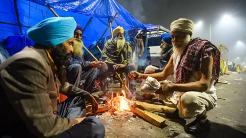 Getty Images Farmer warm themselves around a bonfire at Ghazipur on January 28, 2021