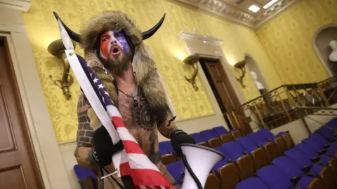 Getty Images A man in horns and a fur hat, alleged to be Jake Angeli, pictured inside the Senate chamber