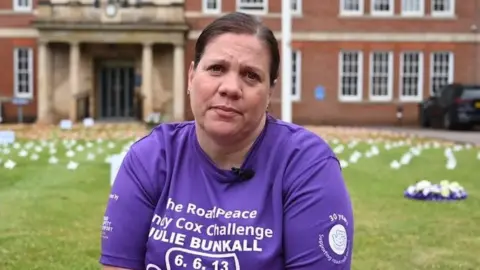 Northamptonshire Police Woman with short dark hair sitting in the grounds of Wootton Hall wearing a purple "Road Peace Challenge" t-shirt