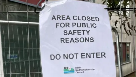 Suki Somal/BBC "Area closed" notice on metal fencing surrounding new building