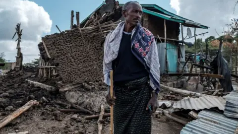 Getty Images A man stands in front of his destroyed house in the village of Bisober in Ethiopia's Tigray region, on December 9, 2020.