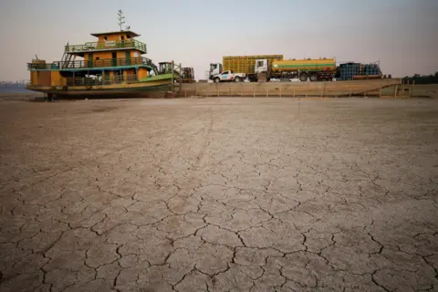 Reuters A tug boat and a barge carrying three trucks, 2,000 empty cooking gas cylinders stranded on a sand bank of a diminished Rio Negro river after running aground last month, as the region is hit by a severe drought, in Cacau Pirera, Brazil October 10, 2023.