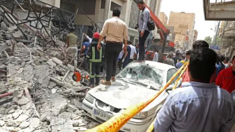 Tasnim News/AFP Rescue workers and bystanders search through the rubble of a collapsed building in Abadan, Iran (23 May 2022)