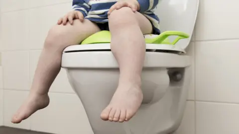 Getty Images A file picture showing the legs of a toddler sitting on a toilet