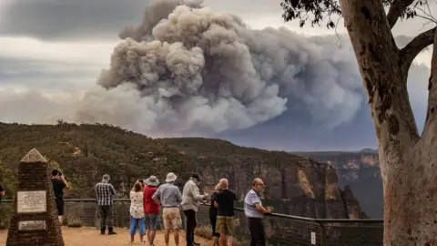 NINA LIPSCOMBE Tourists at a vantage point in the Blue Mountains look at huge smoke clouds from a bushfire