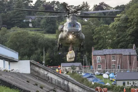 RAF/MOD handout Chinook helicopter approaches with the load to drop on the dam in Whaley Bridge