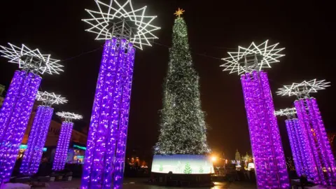 Petro Poroshenko The Christmas tree is tall and thin. It is cone-shaped with few branches visible.