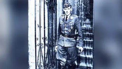 FAMILY PHOTO Decorated Luftwaffe pilot Güenter Brixius walks down some steps and through a gate in full uniform